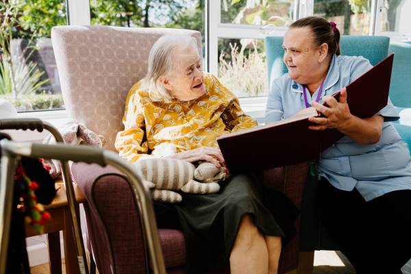 An elderly woman is being read a story by a social care worker in a residential care home.