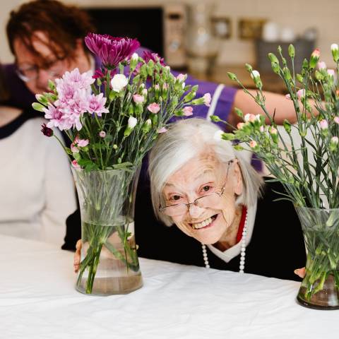 An elderly lady happily looks through flowers.
