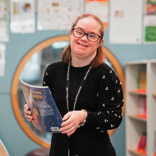 The image shows a young lady with down syndrome smiling while holding a magazine.