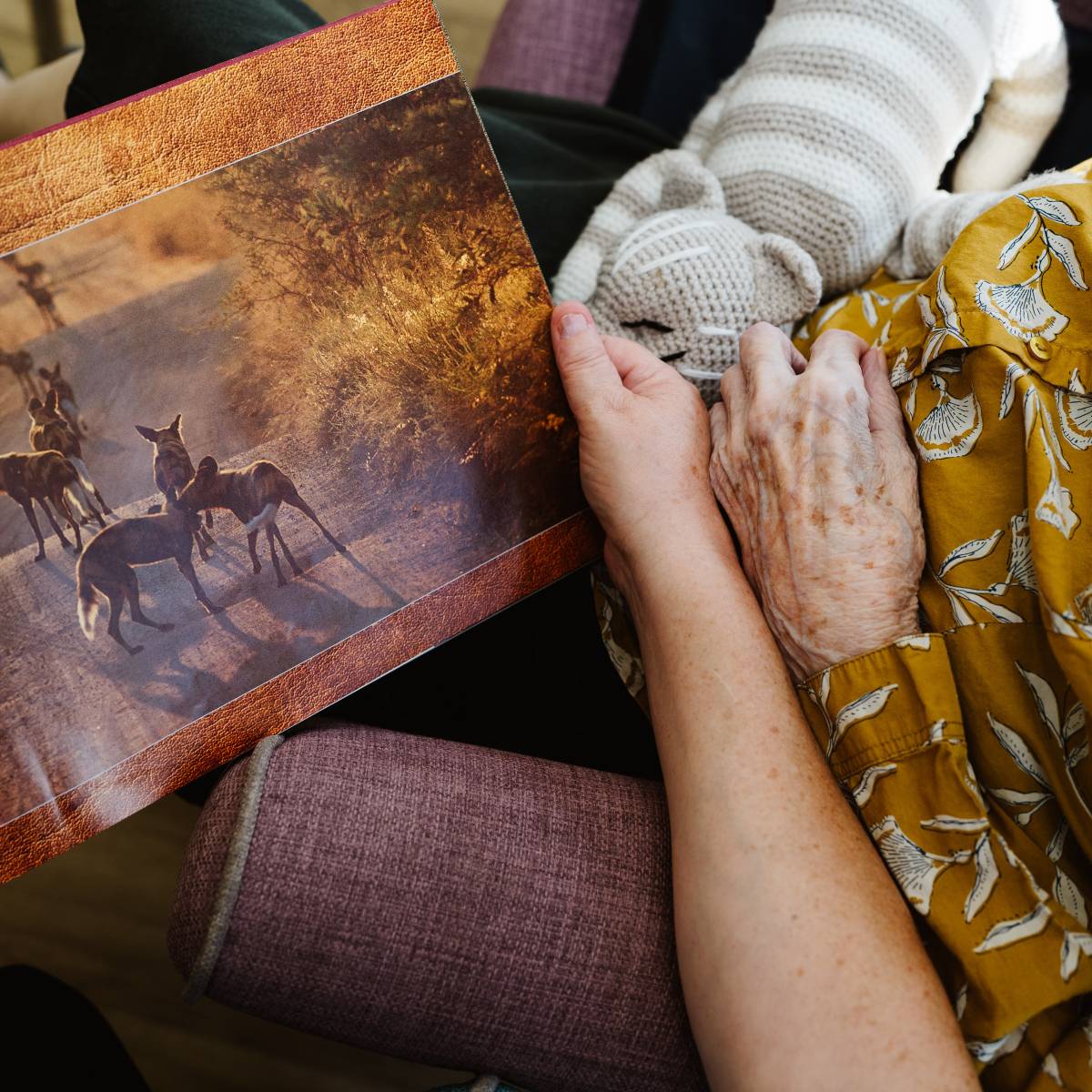 The photo shows the arm of someone holding open a book with an arm of an elderly person next to it.